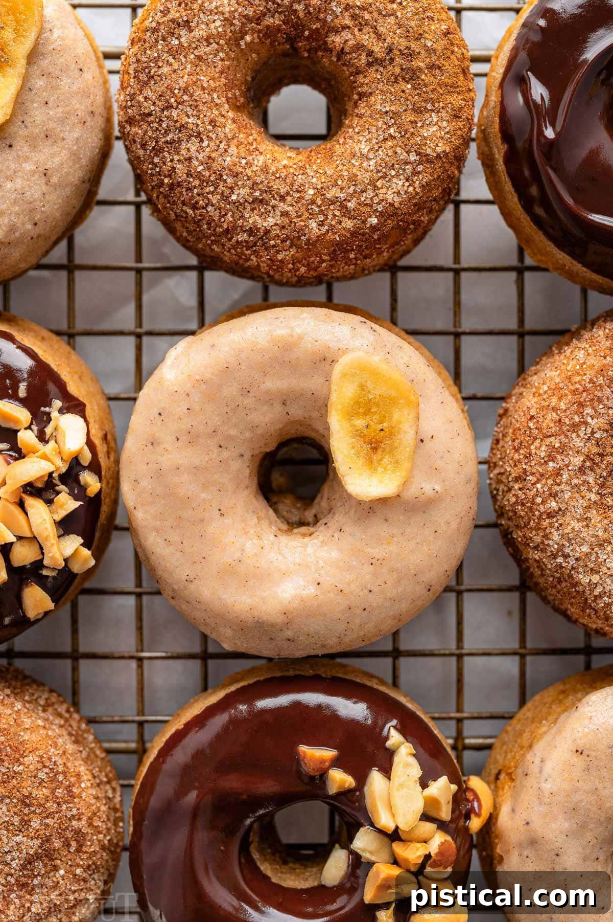 Delightful Banana Doughnuts 2 A top down view of banana donuts with various toppings including chocolate, cinnamon sugar, and brown butter glaze, all arranged on a metal cooling rack.