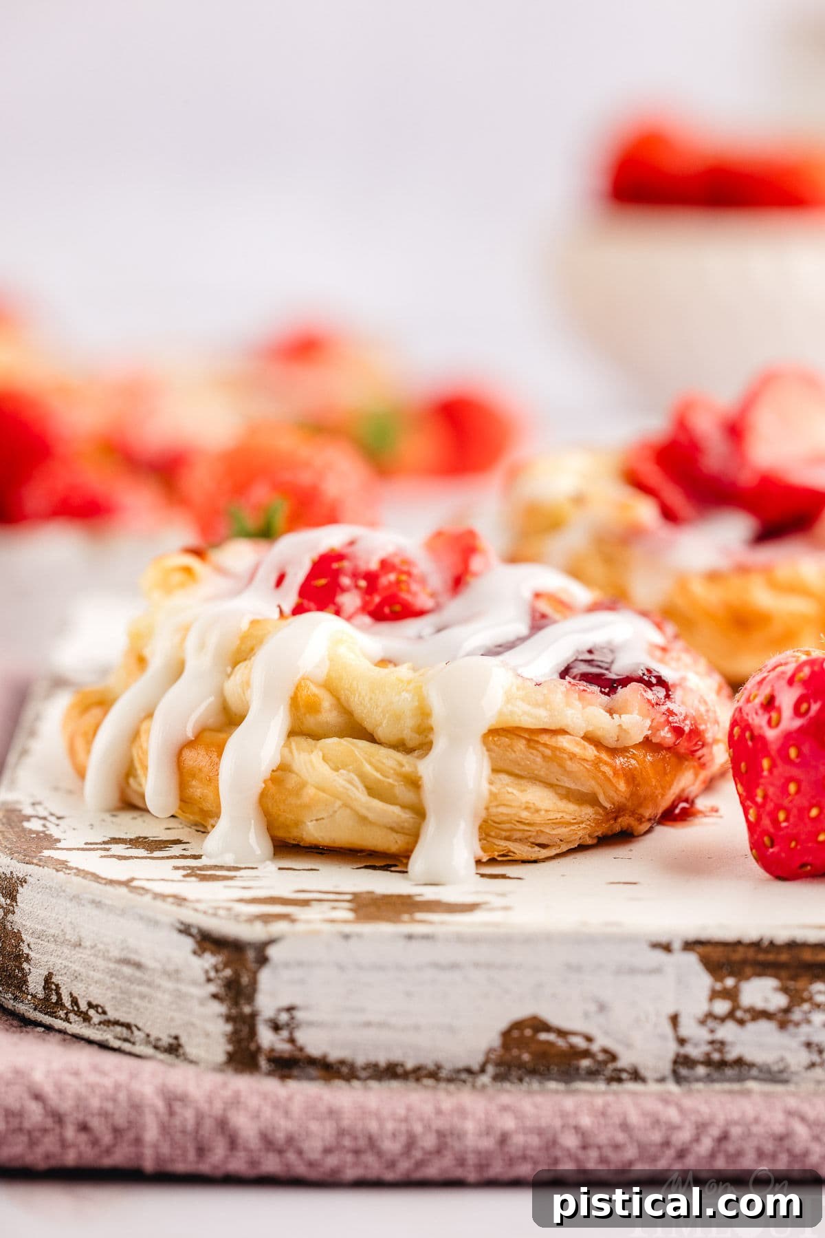 A perfectly baked strawberry cream cheese danish, beautifully drizzled with glaze, resting on a rustic white wooden board, ready to be served.