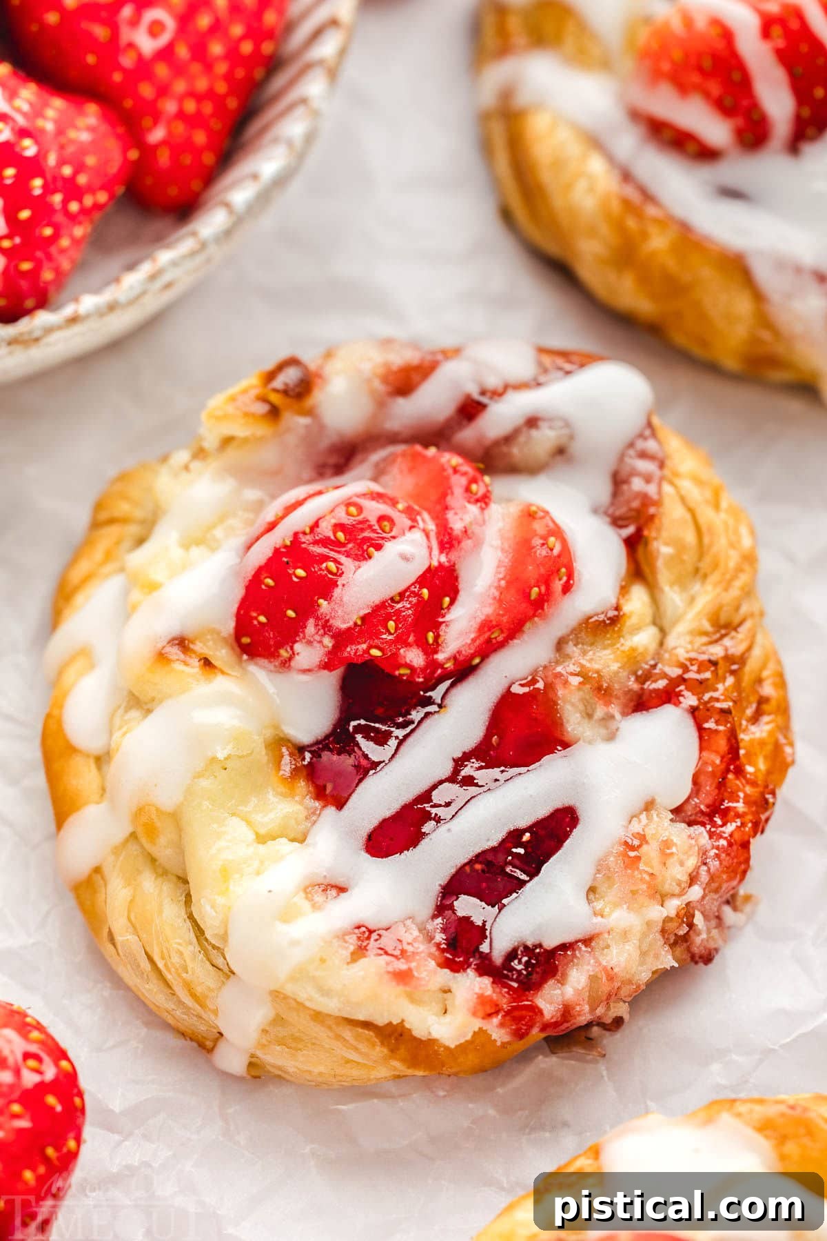 A close-up shot of an easy strawberry danish with a flaky crust, creamy filling, sweet glaze, and fresh strawberry slices, emphasizing its inviting texture and deliciousness.