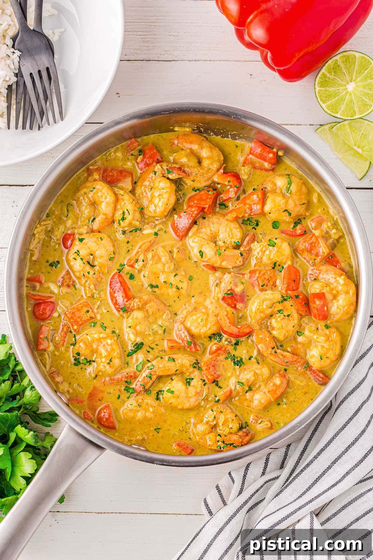 A rustic cast-iron skillet filled with simmering Shrimp Curry, surrounded by fresh ingredients like bell peppers, shallots, and limes, alongside serving plates, highlighting its one-pan simplicity and appeal.