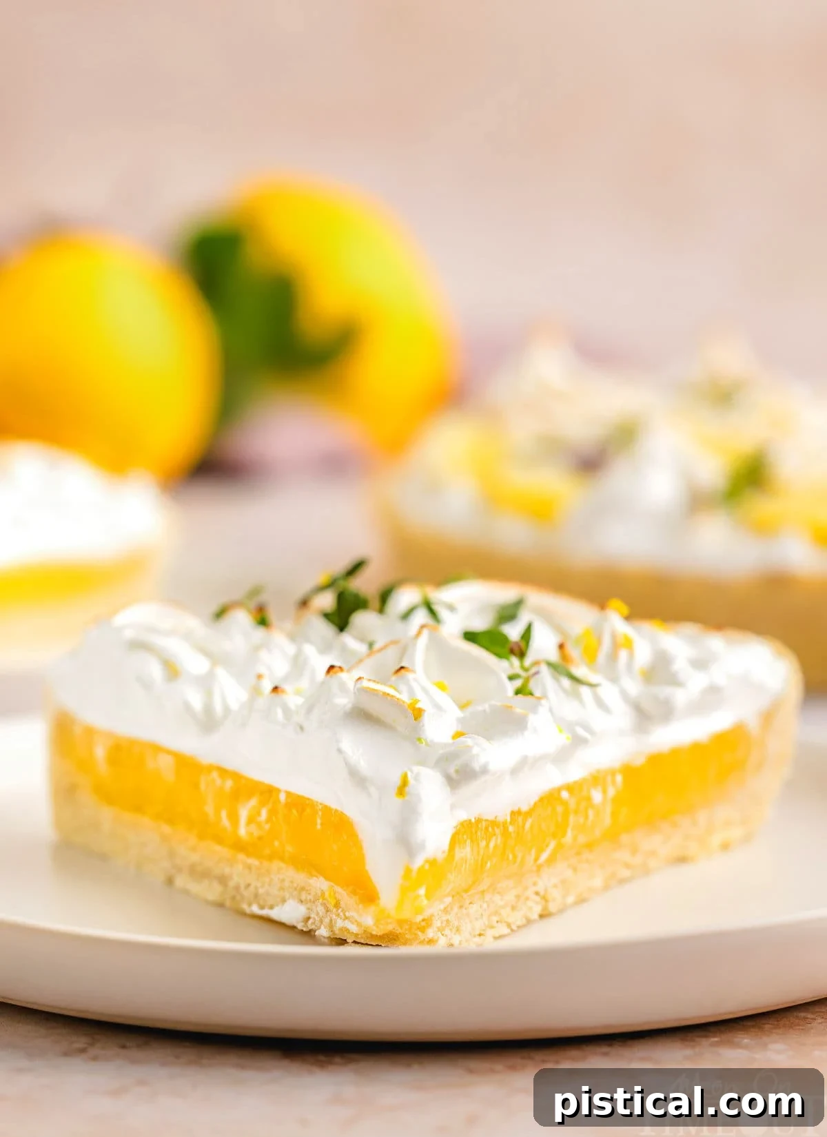 Zesty Lemon Cloud Tart 2 A beautiful slice of Lemon Meringue Tart, showcasing distinct layers of golden crust, vibrant yellow lemon filling, and fluffy toasted meringue, rests on a white plate. More slices and fresh lemons are softly blurred in the background.