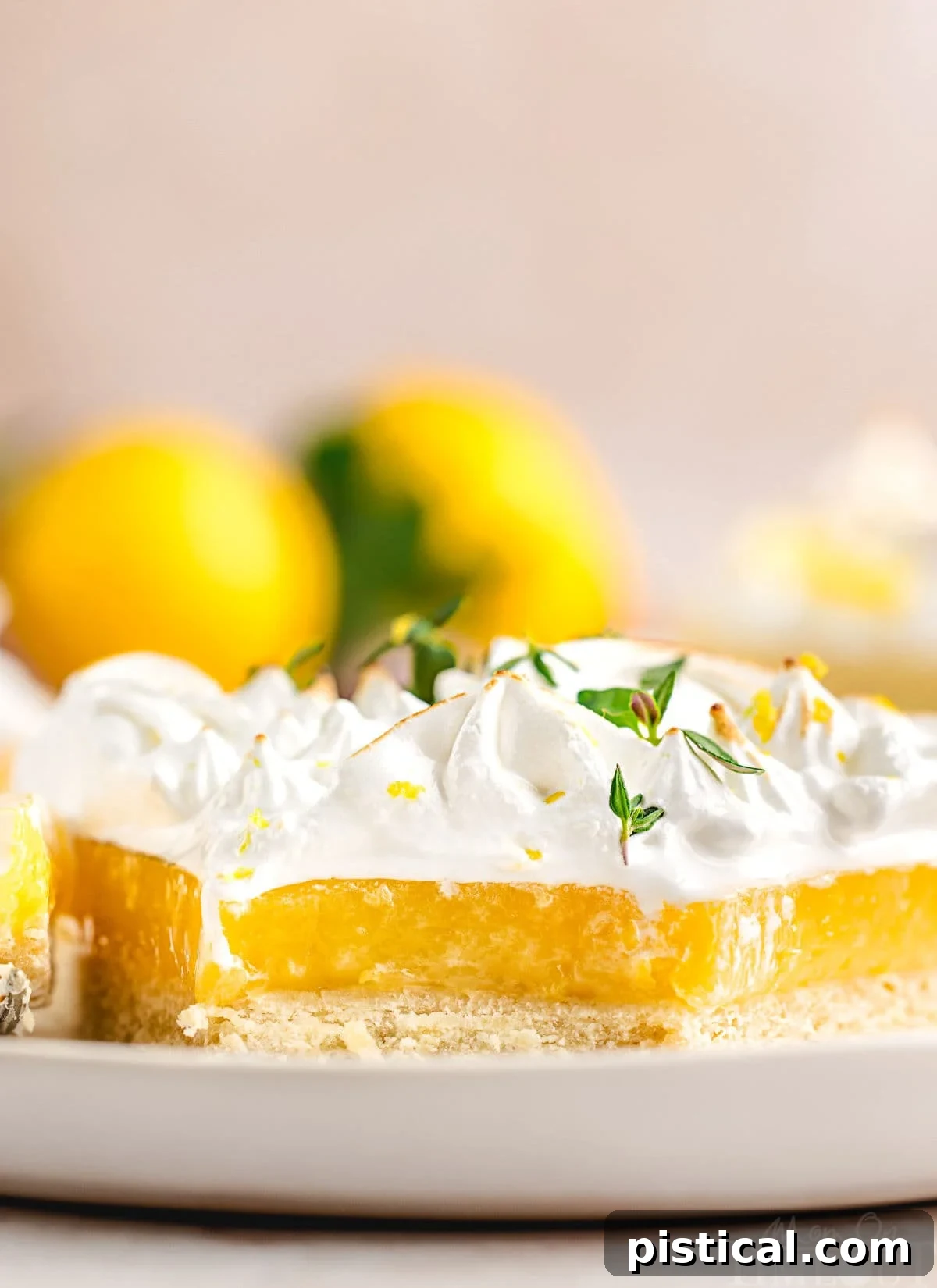 Zesty Lemon Cloud Tart 7 A close-up side view of a slice of Lemon Meringue Tart on a white plate, with a bite taken out, revealing the creamy lemon filling and flaky crust. Fresh lemons are blurred in the background.