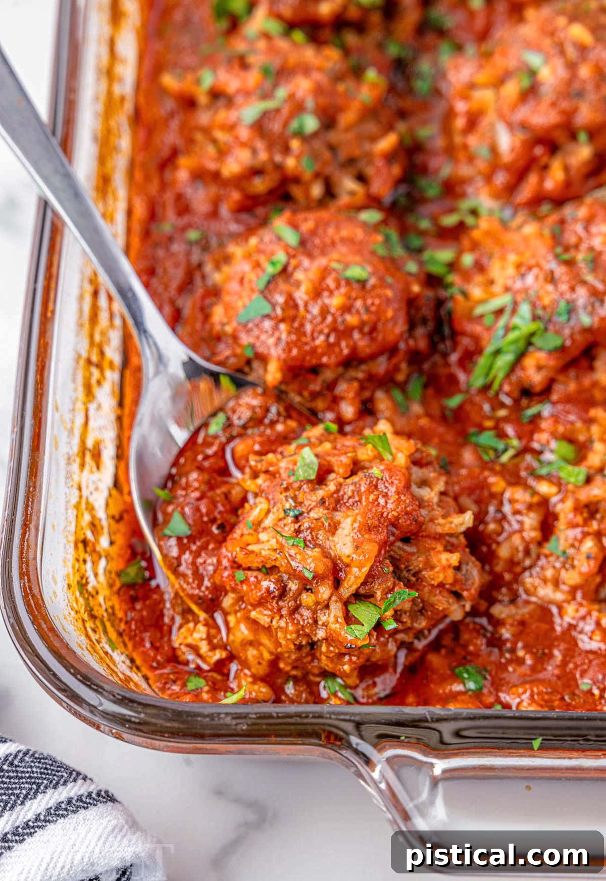Porcupine meatballs nestled in a vibrant red tomato sauce in a glass baking dish, with a metal spoon lifting one out.