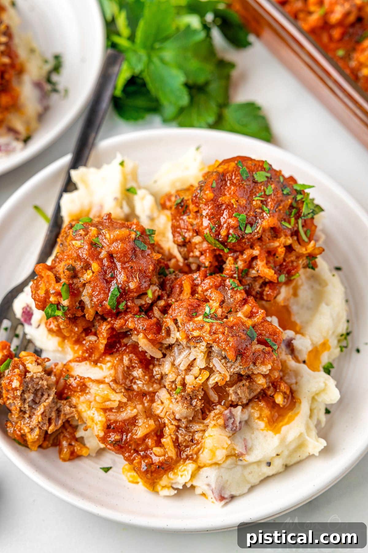 Three perfectly formed meatballs resting on a bed of creamy mashed potatoes on a white plate, garnished with fresh herbs.