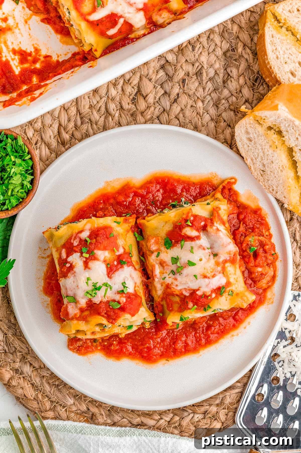 Top down look at two lasagna roll ups on a plate next to the casserole dish.