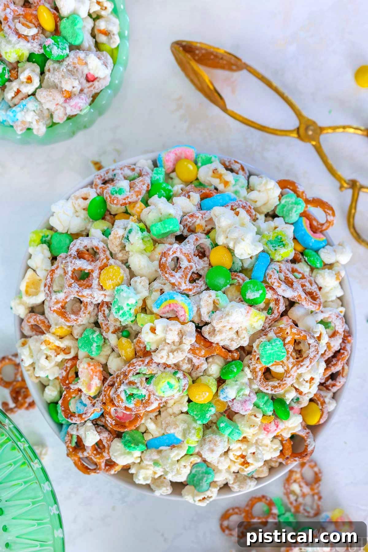 Top down view of Leprechaun Bait snack mix in white round bowl. Brass tongs are sitting next to the bowl.