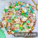 Top down view of Leprechaun Bait snack mix in white round bowl. Brass tongs are sitting next to the bowl.