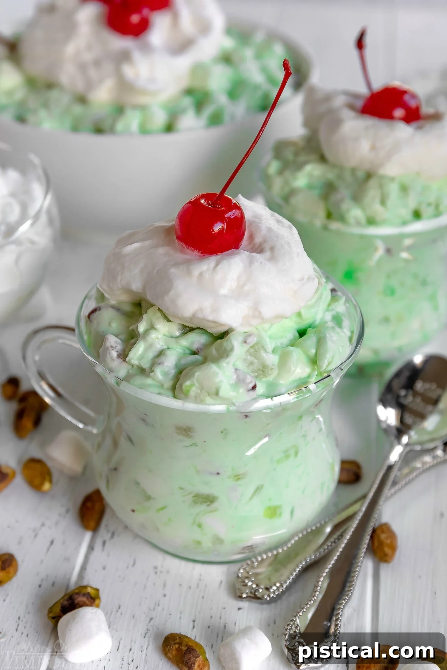 Watergate Salad topped with whipped cream and a maraschino cherry, garnished with chopped pistachios, ready for serving.