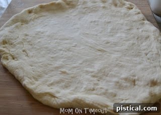 Pizza dough being stretched and shaped on a lightly floured surface for a pizza pan.