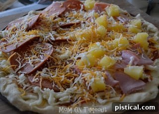 Prepared pizza on a pizza pan, ready for baking. Shows light greasing and cornmeal dusting.
