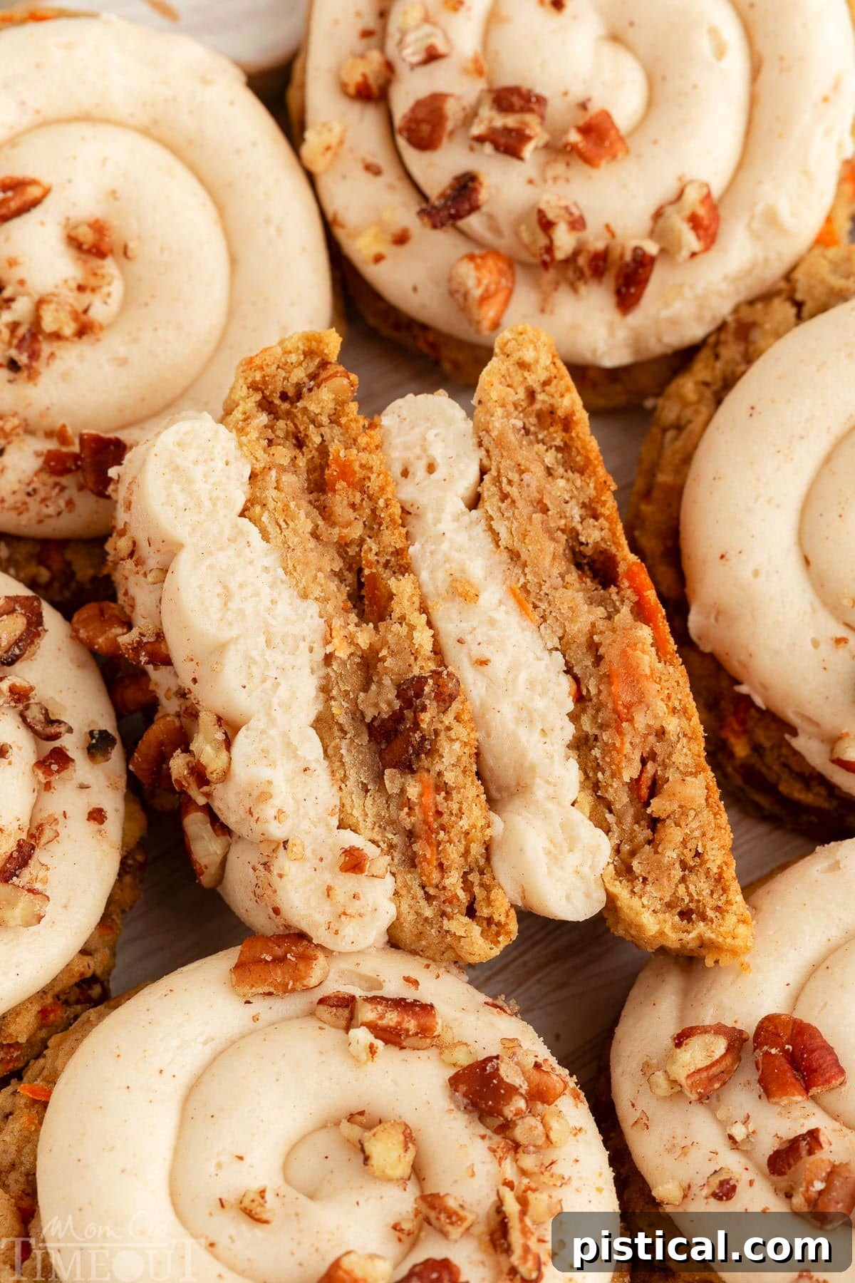Cream Cheese Frosted Carrot Cookies 2 A carrot cake cookie cut in half to show the soft, moist texture inside, adorned with creamy frosting. Several whole cookies are artfully arranged around it.