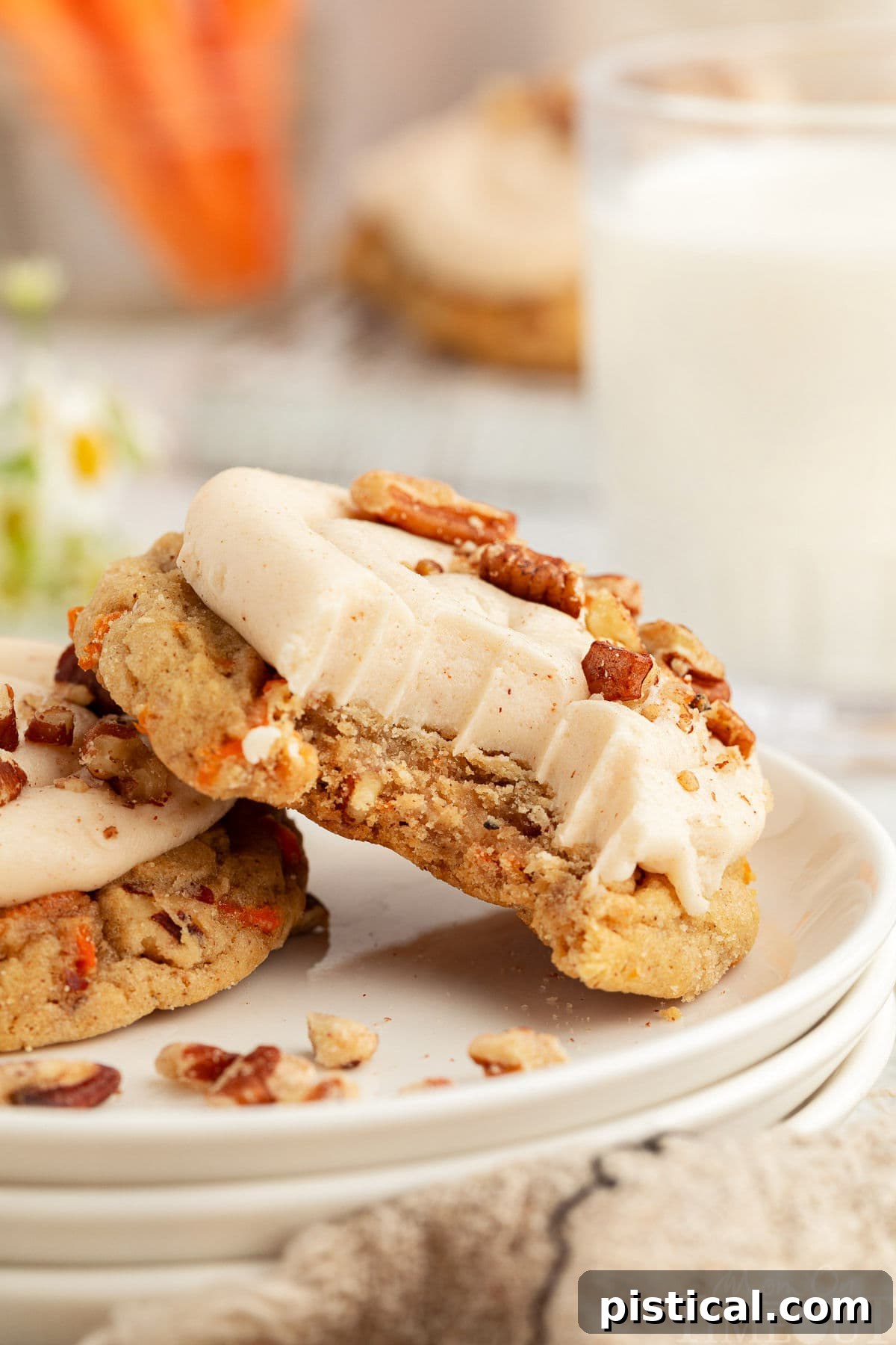 Cream Cheese Frosted Carrot Cookies 8 A delectable Carrot Cake Cookie with a bite taken out, revealing its soft interior, resting against another cookie on a pristine white plate.