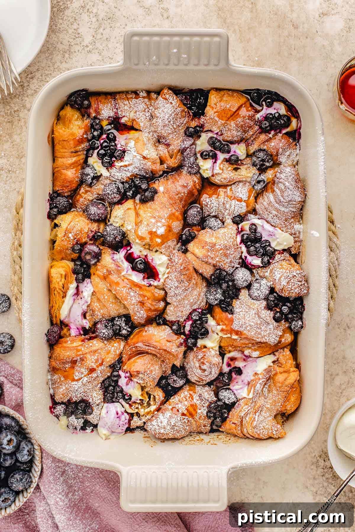 Luscious Blueberry Croissant French Toast Bake 2 Top down look at croissant french toast bake in baking dish made with blueberries and topped with a dusting of powdered sugar.