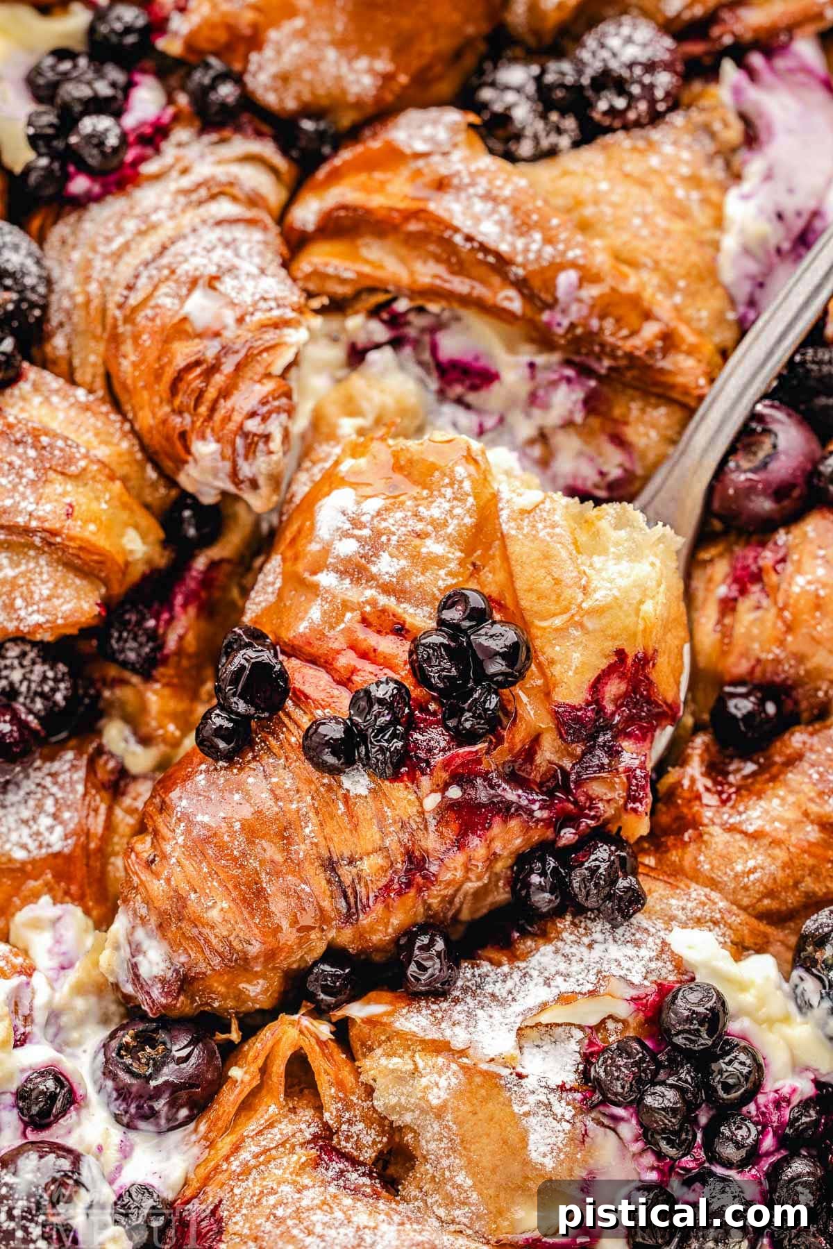 Luscious Blueberry Croissant French Toast Bake 11 Piece of blueberry croissant french toast bake being lifted out of the casserole dish.