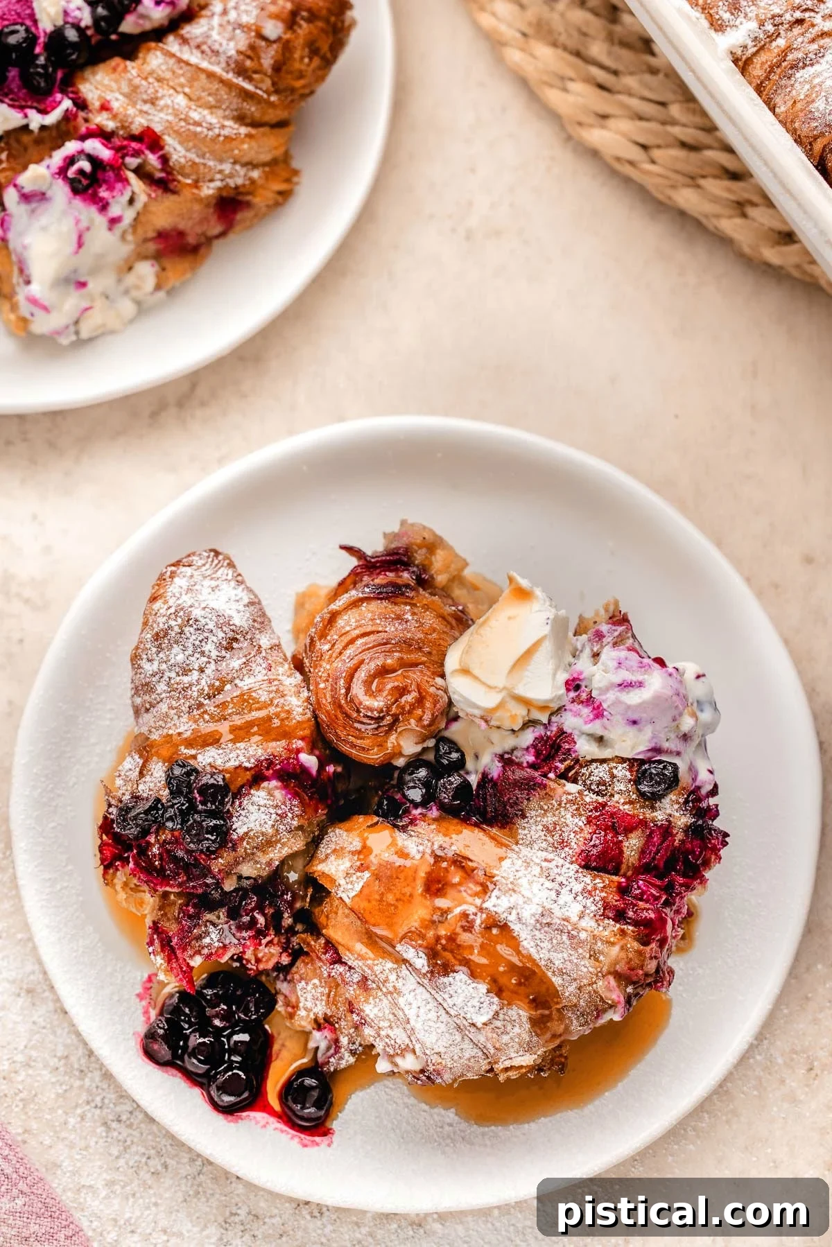 Luscious Blueberry Croissant French Toast Bake 3 Top down look at Blueberry croissant bake recipe on white round plate topped with maple syrup.