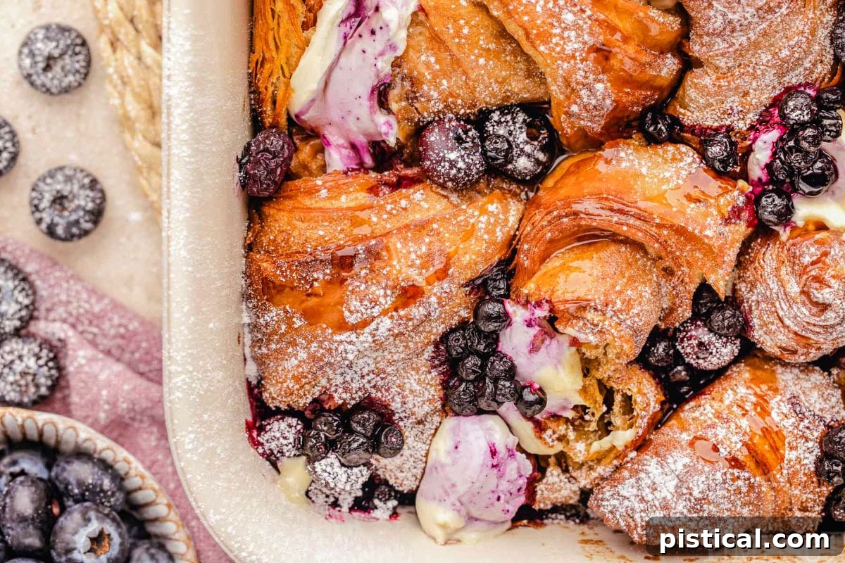 Luscious Blueberry Croissant French Toast Bake 7 Wide look at the corner of the baking dish with freshly baked blueberry croissant french toast bake recipe. Blueberries can be seen on the side of the baking dish.
