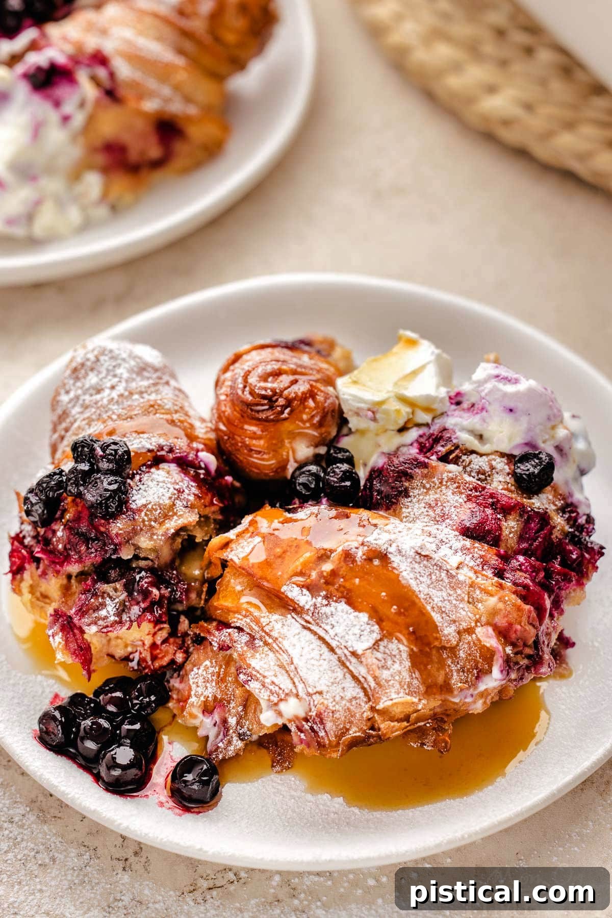 Luscious Blueberry Croissant French Toast Bake 8 Blueberry croissant bake recipe on white round plate topped with maple syrup.
