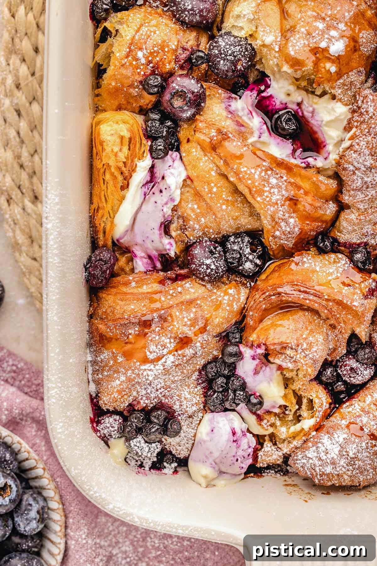 Luscious Blueberry Croissant French Toast Bake 10 Top down look at croissant french toast bake in baking dish made with blueberries and topped with a dusting of powdered sugar.