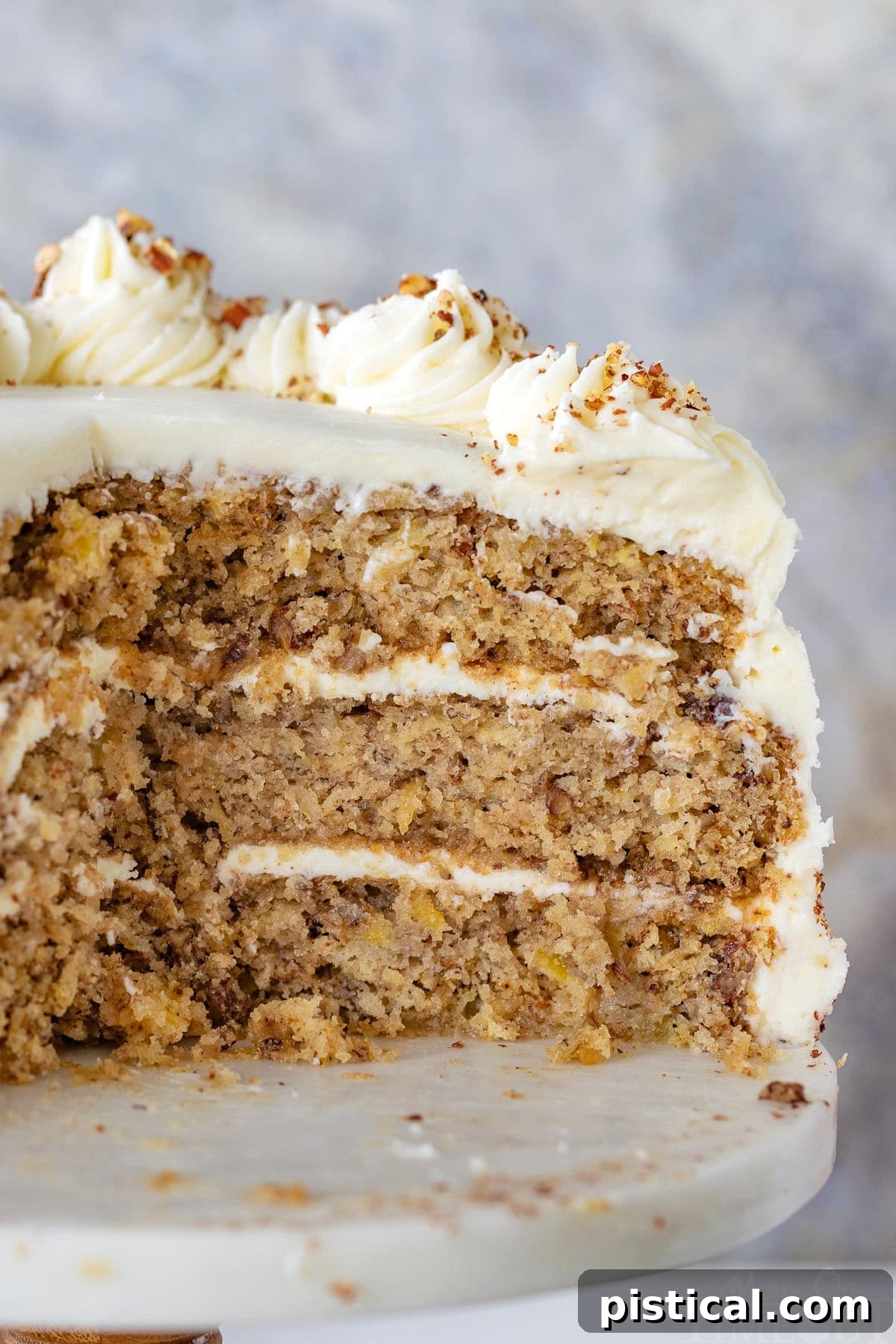 A clear cross-section view of the Hummingbird Cake recipe, proudly displayed on a white cake stand, highlighting its moist layers and generous frosting.