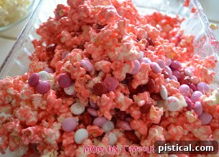 Sweetheart Popcorn Bites 8 Mixing popcorn with marshmallow mixture by hand, wearing baking spray for protection.