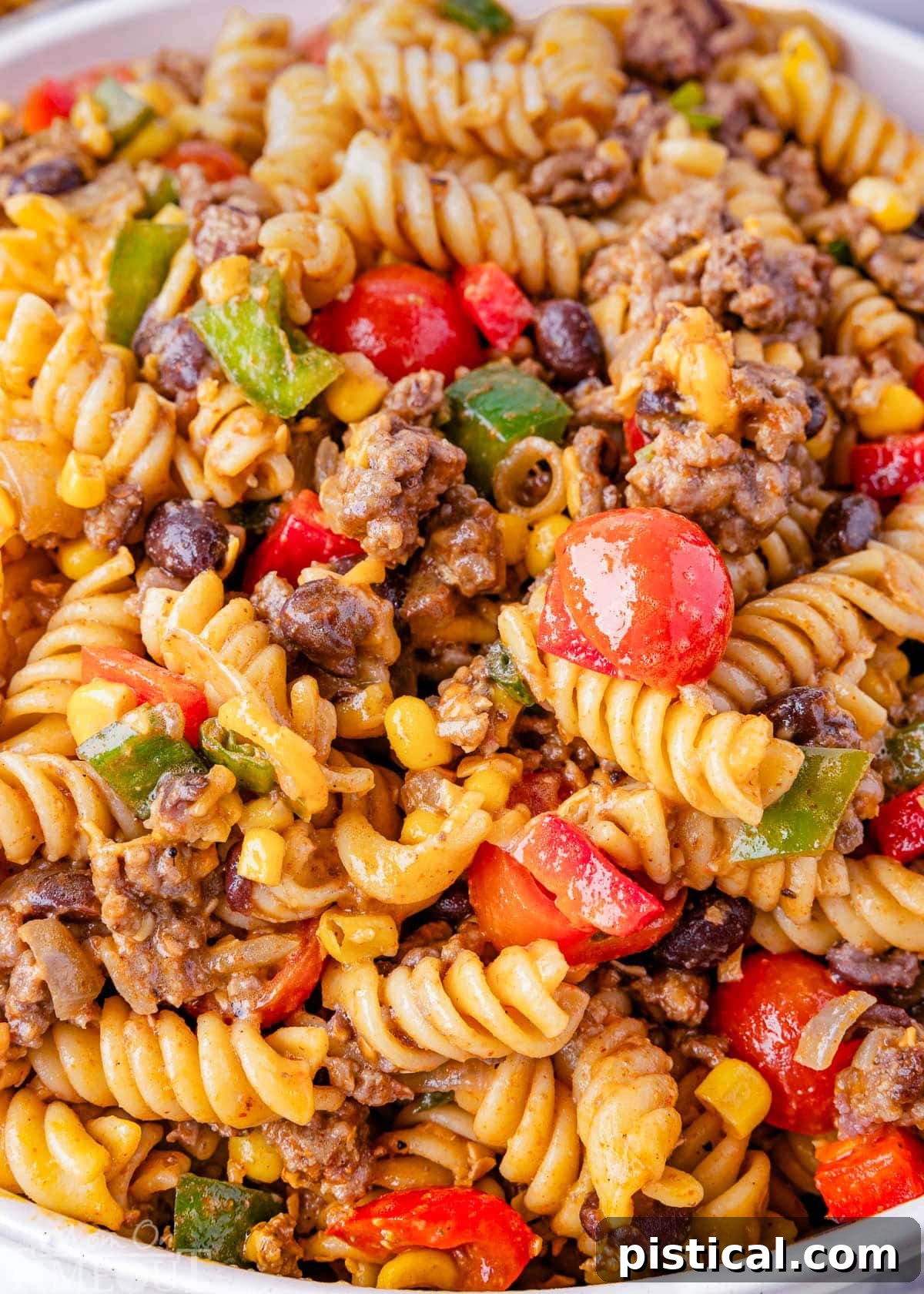 Ranch Hand Pasta Salad 5 A close-up shot of the Cowboy Pasta Salad, highlighting the individual components: tender cherry tomatoes, seasoned ground beef, spiral pasta, crisp bell peppers, savory cheddar cheese, and fresh green onions, all beautifully coated in a zesty lime and taco dressing.