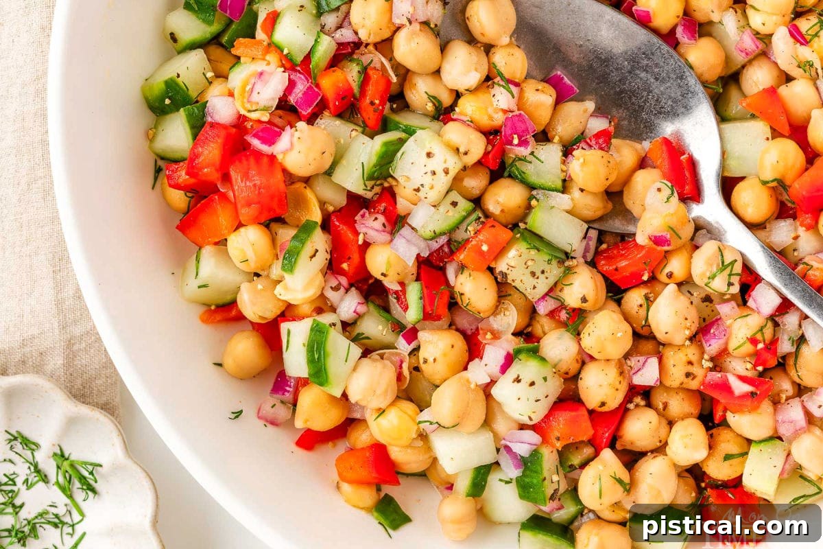 Wide shot of garbanzo bean salad in white bowl with serving spoon.