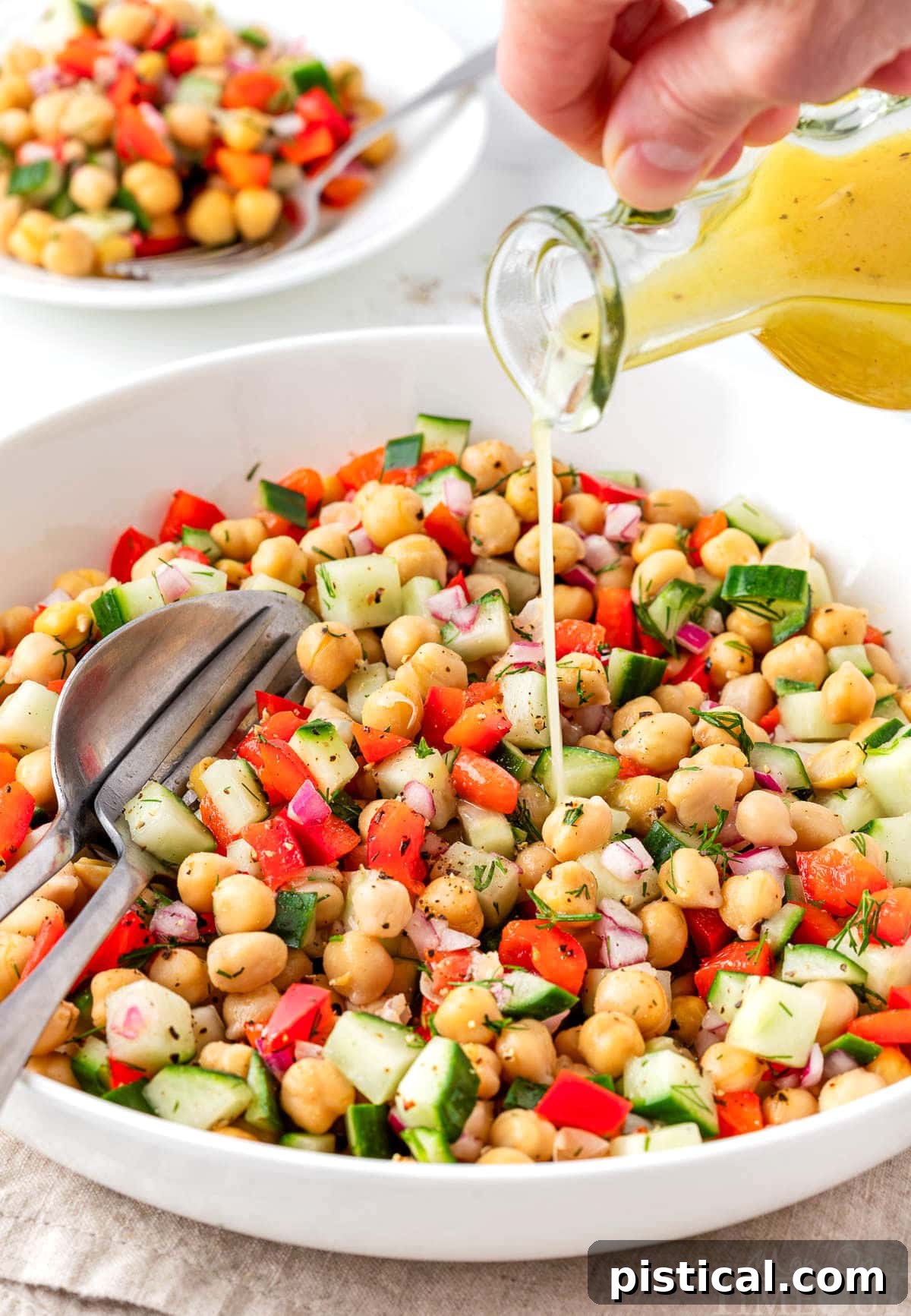Dressing being poured over chick pea salad in a white bowl.