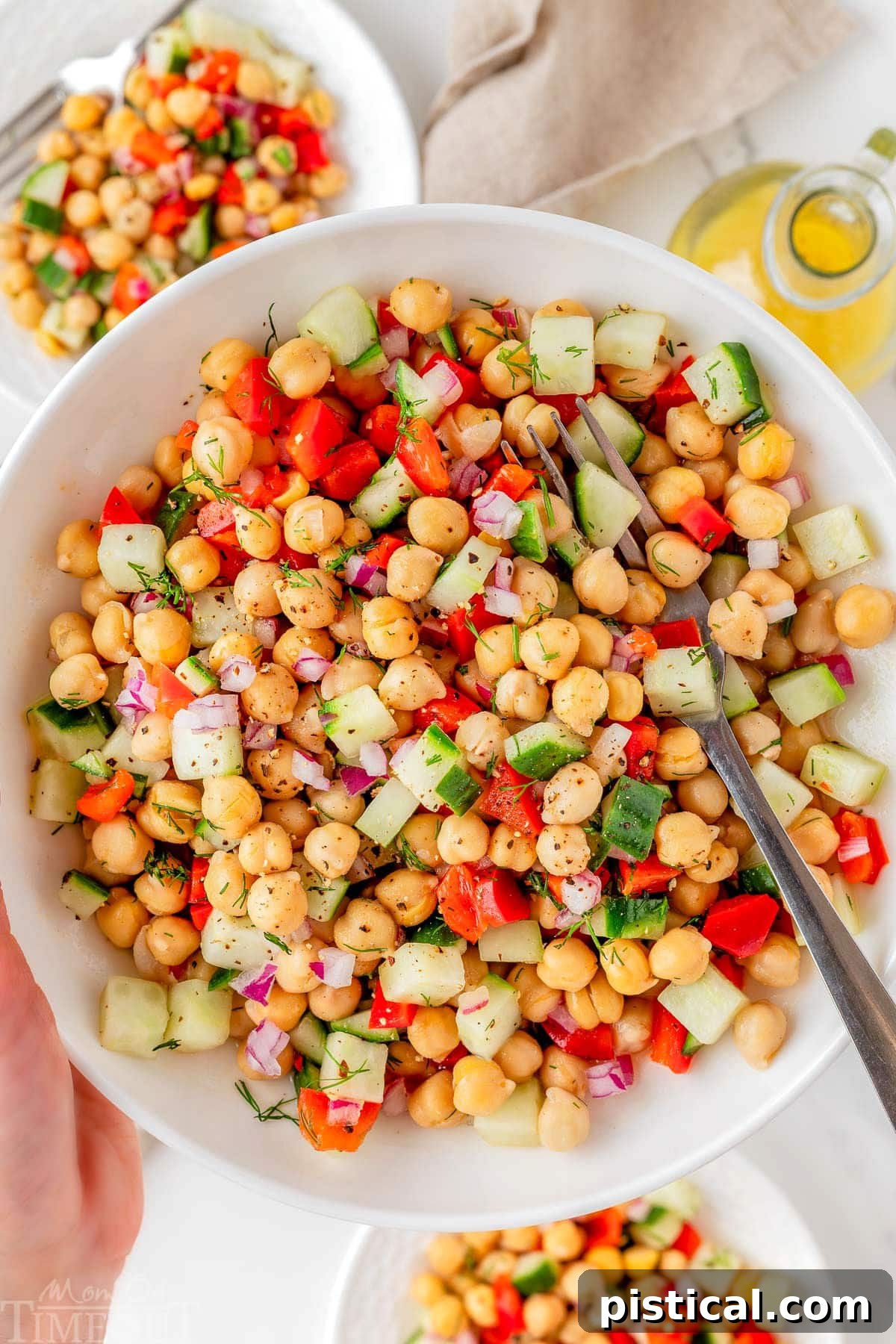 Bowl of chickpea salad recipe being held up over two small plates with the salad on them.