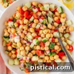 Bowl of chickpea salad recipe being held up over two small plates with the salad on them.