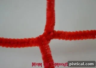 A Hershey's Kiss placed at the center of the pipe cleaner 'X'.