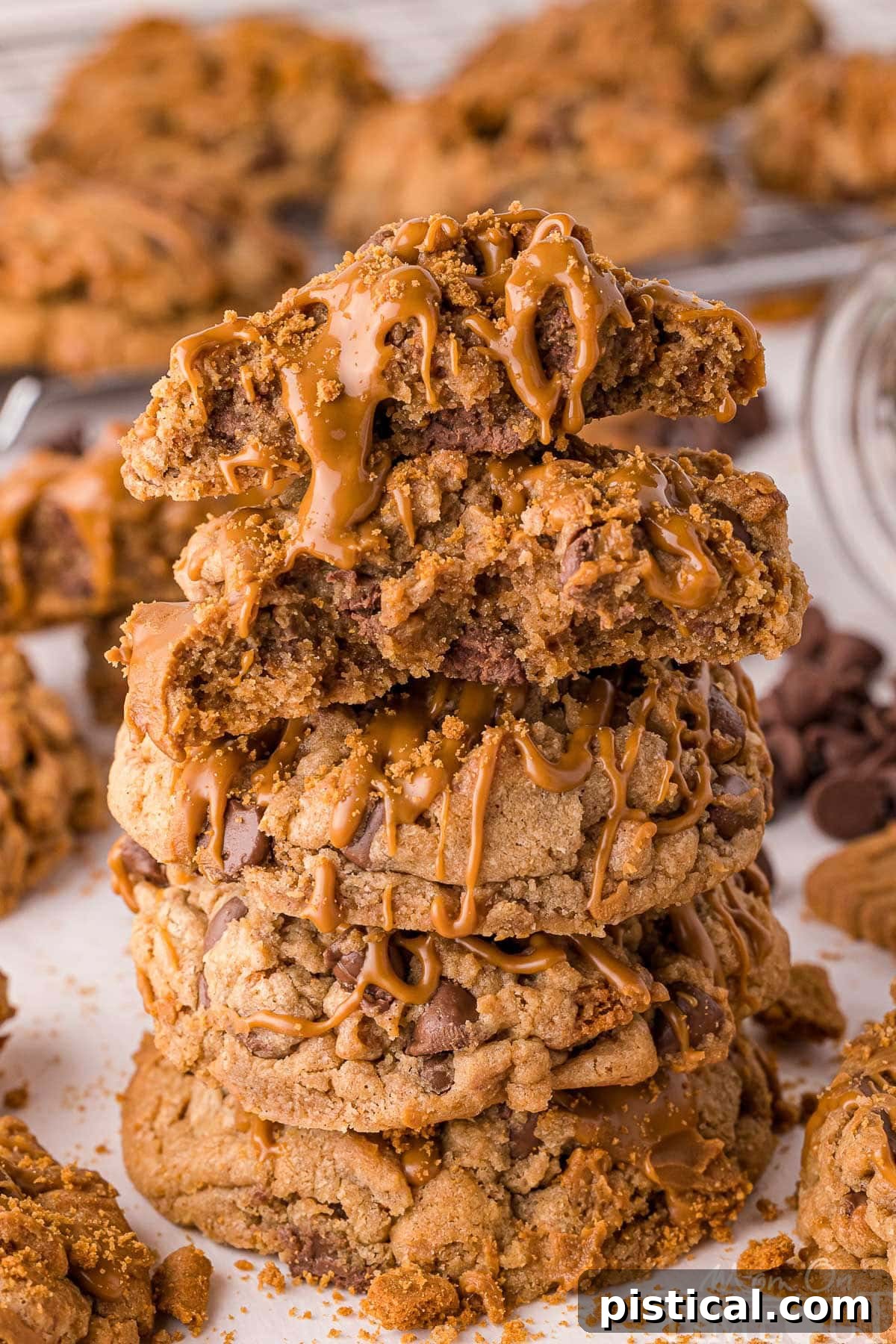 Ultimate Biscoff Chocolate Chip Cookies 8 Stack of four biscoff chocolate chip cookies topped with cookie butter stacked on white parchment. Top cookie is broken in half. More cookies can be seen in the background.
