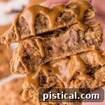 Ultimate Biscoff Chocolate Chip Cookies 9 Two biscoff cookies broken in half and topped with cookie butter held in a hand.