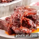 Shot of st louis ribs on white round plate with the rest of the party ribs in a foil pan in the background.