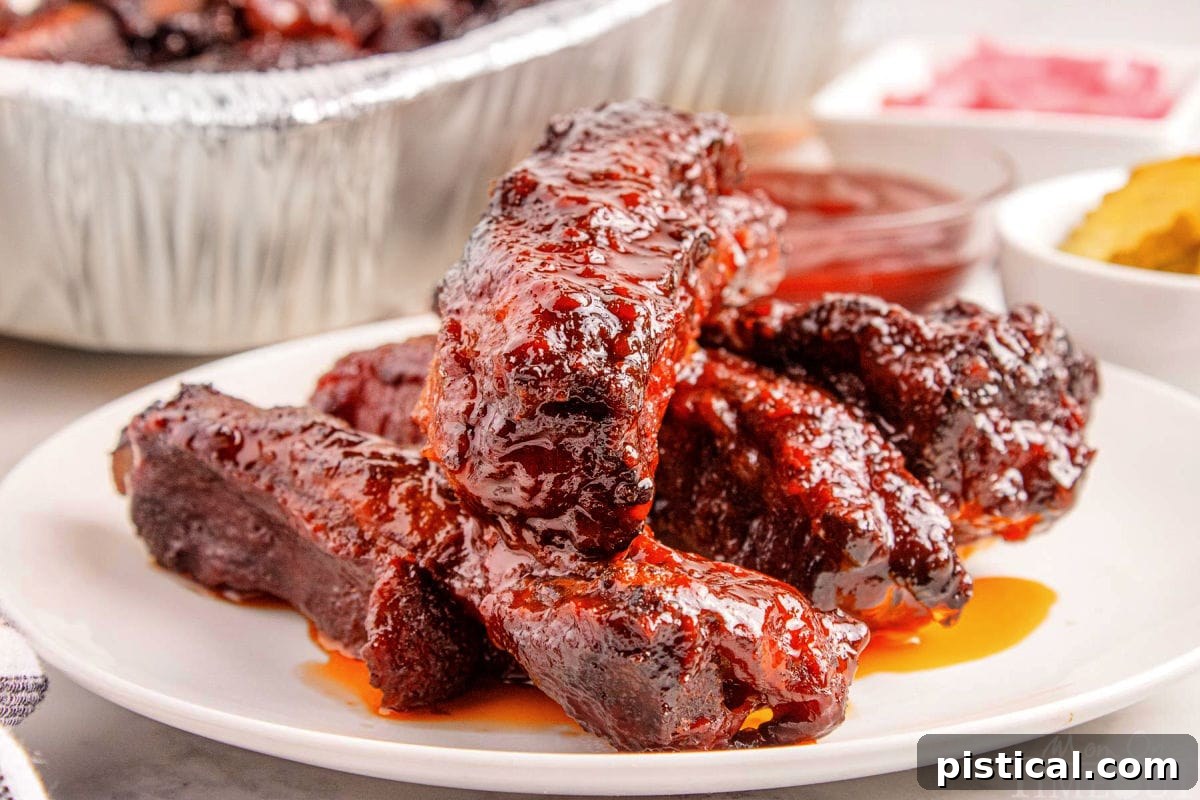 Shot of st louis ribs on white round plate with the rest of the party ribs in a foil pan in the background.