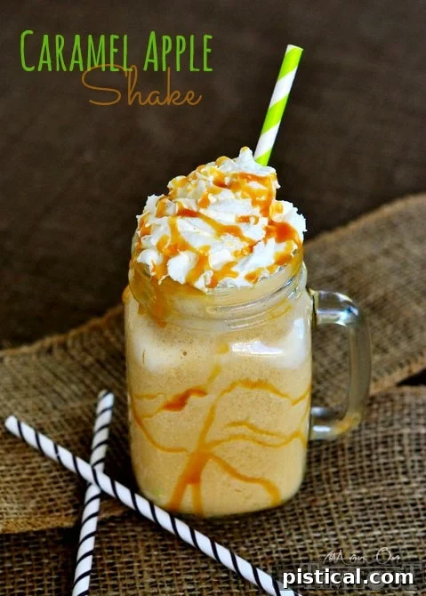 A tall glass of Caramel Apple Shake, topped with whipped cream and caramel, on a wooden surface. | MomOnTimeout.com