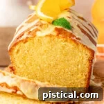 Front view of orange pound cake on wood cutting board with two slices cut off.