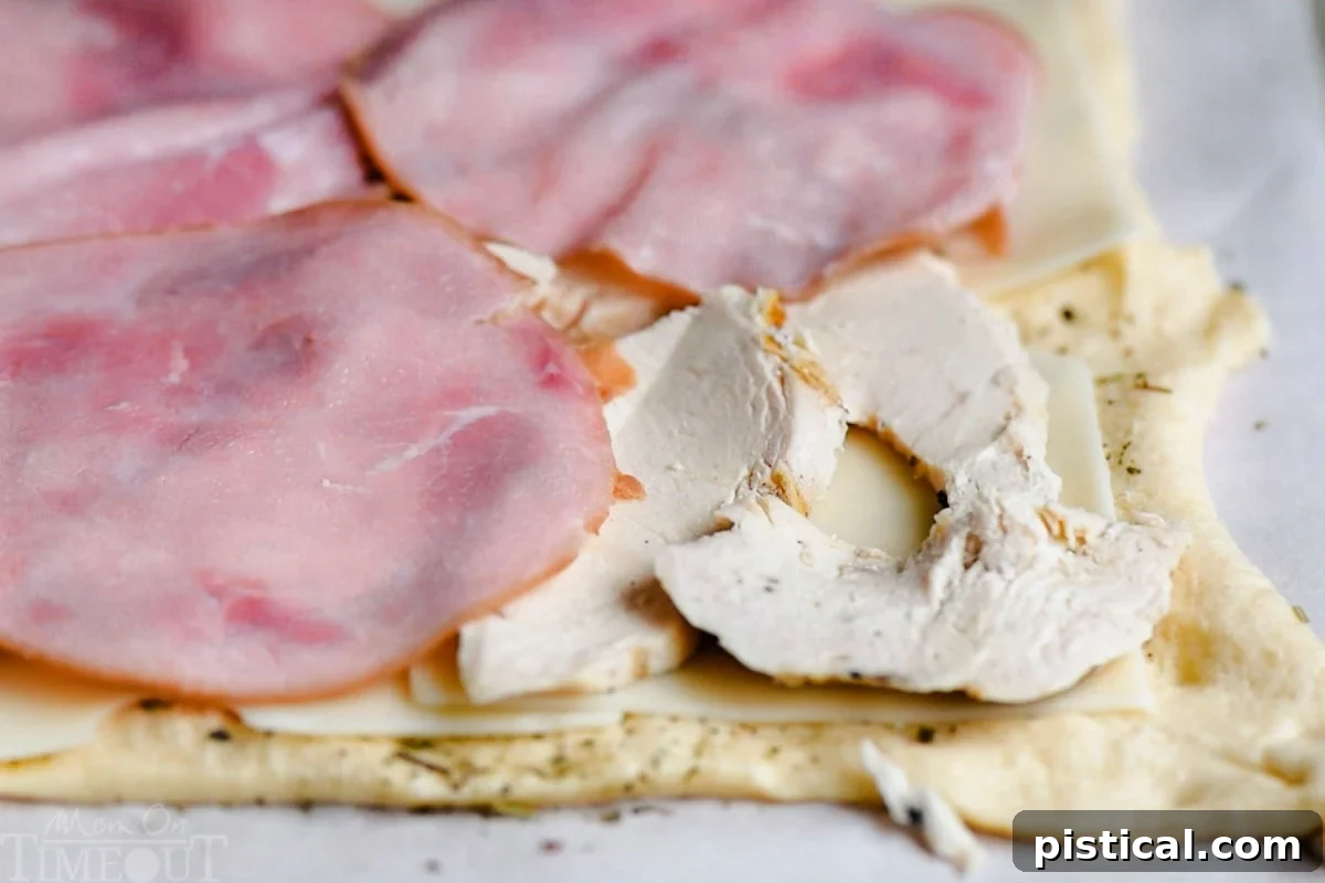 Close-up shot showing the layers of crescent dough, Swiss cheese, thinly sliced chicken, and ham before rolling.