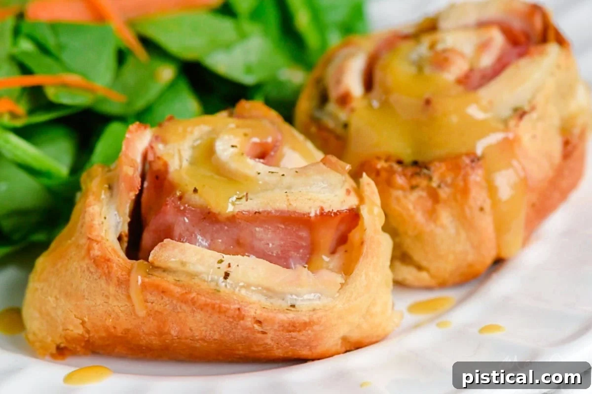 Chicken Cordon Bleu Crescent Rolls served on a plate with honey Dijon sauce drizzled on top, alongside a fresh green salad.