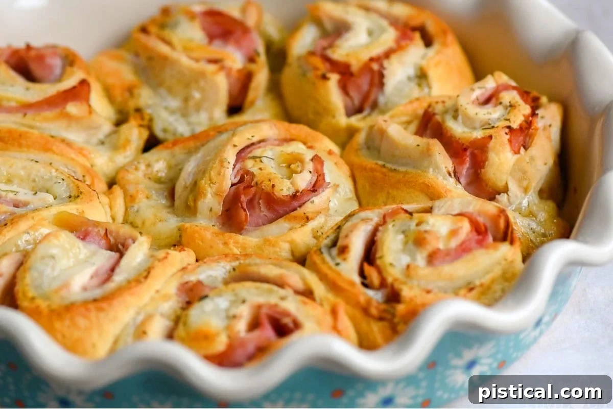 Wide shot of several chicken cordon bleu crescent roll ups arranged in a white pie dish, freshly baked.