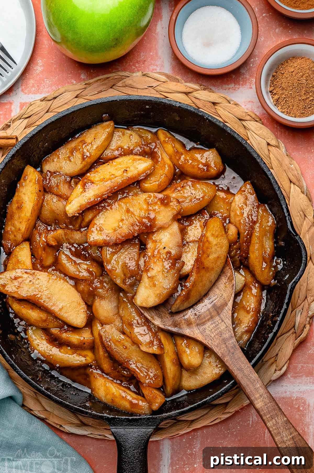 Overhead shot of fried apples in cast iron skillet. Spices and sugar in small bowls around it. 