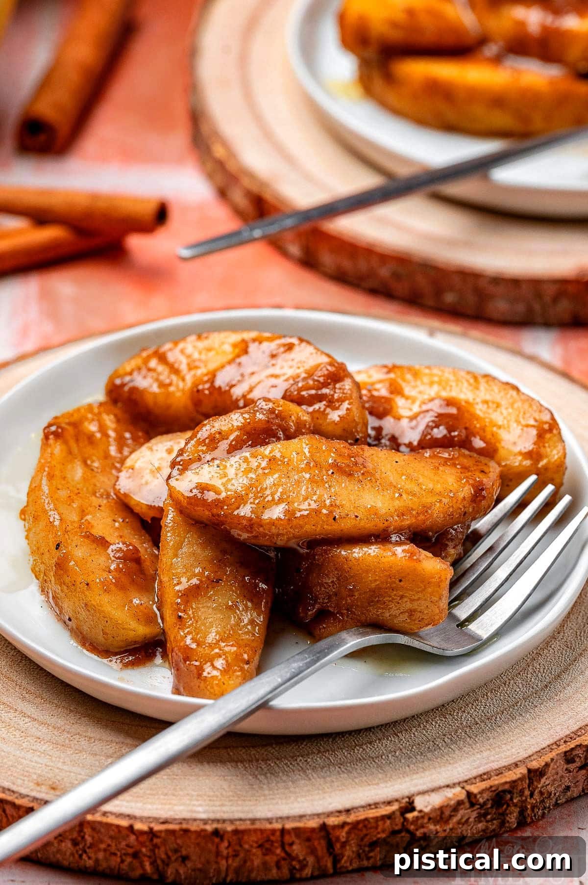 Serving of fried apples on a small white round plate with a fork resting on the edge.