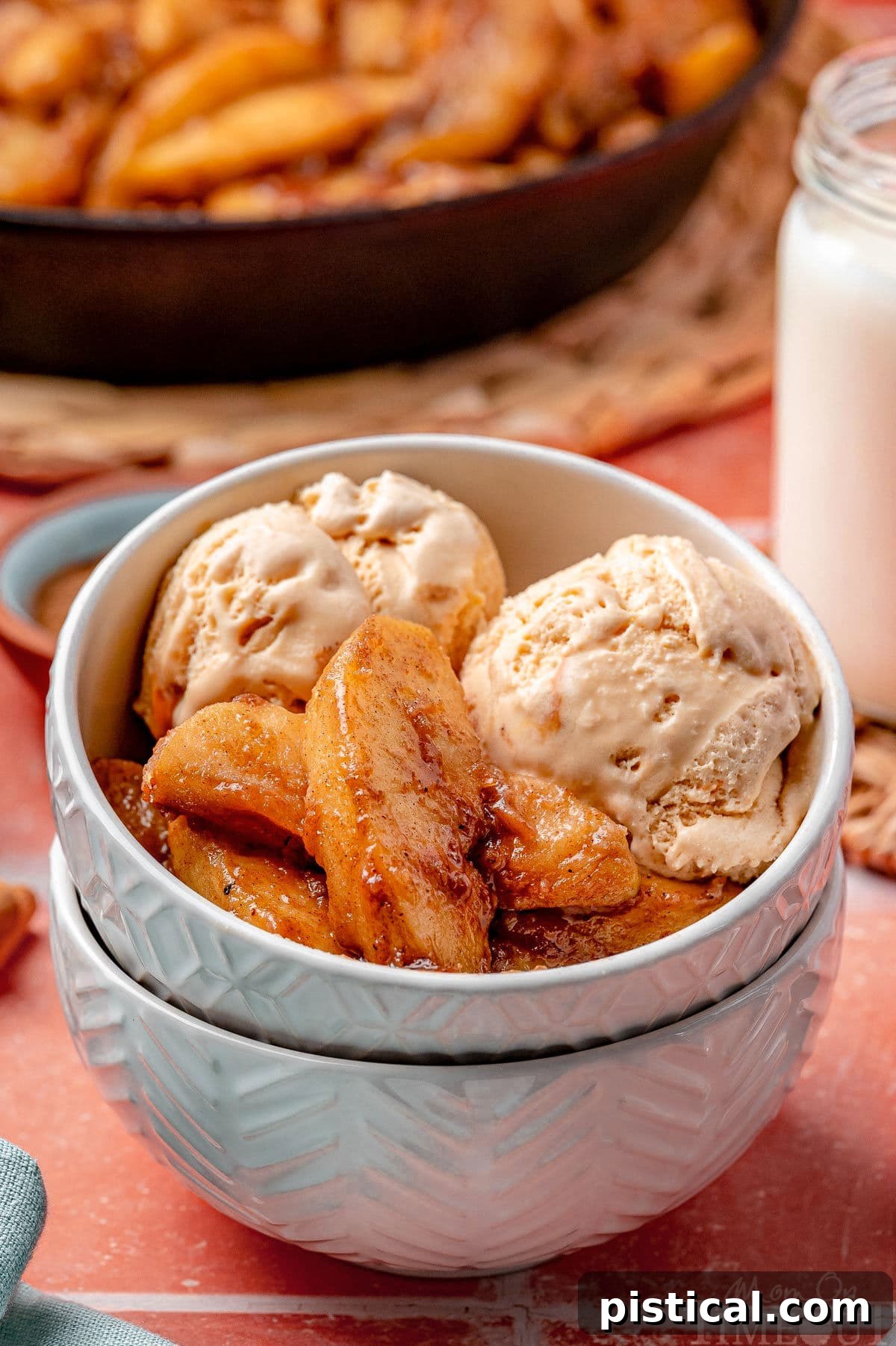 Fried apple recipe served with ice cream in small bowl that is stacked in another bowl. Glass of milk and cast iron skillet can be seen in the background.