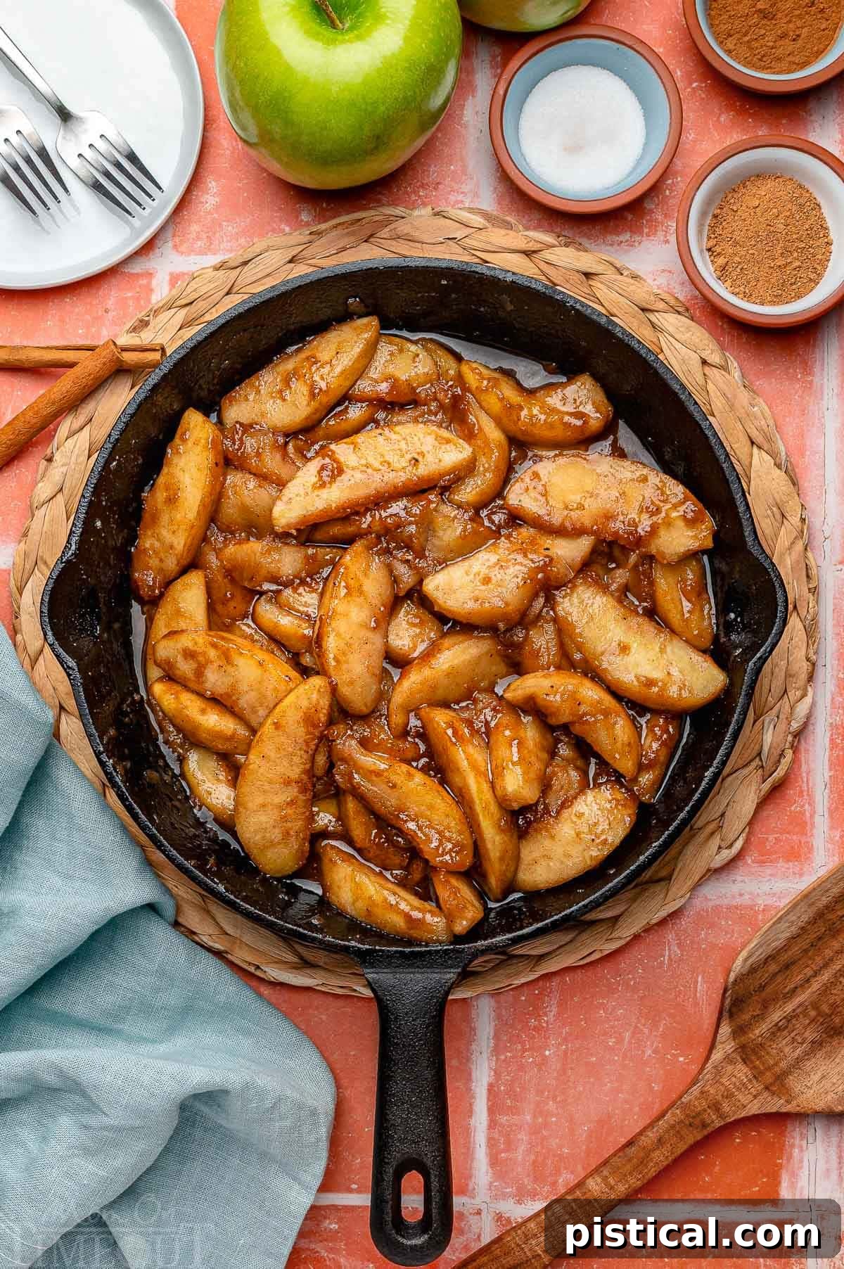 Overhead shot of fried apples in cast iron skillet. Spices and sugar in small bowls around it.