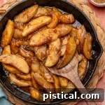 Overhead shot of fried apples in cast iron skillet. Spices and sugar in small bowls around it.