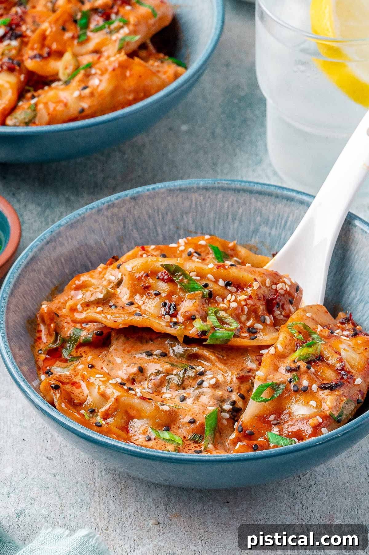 Crispy Sheet Pan Dumplings 7 A bowl brimming with delicious baked dumplings, beautifully garnished with vibrant green onions, a sprinkle of sesame seeds, and a tempting drizzle of chili crisp, ready to be enjoyed.