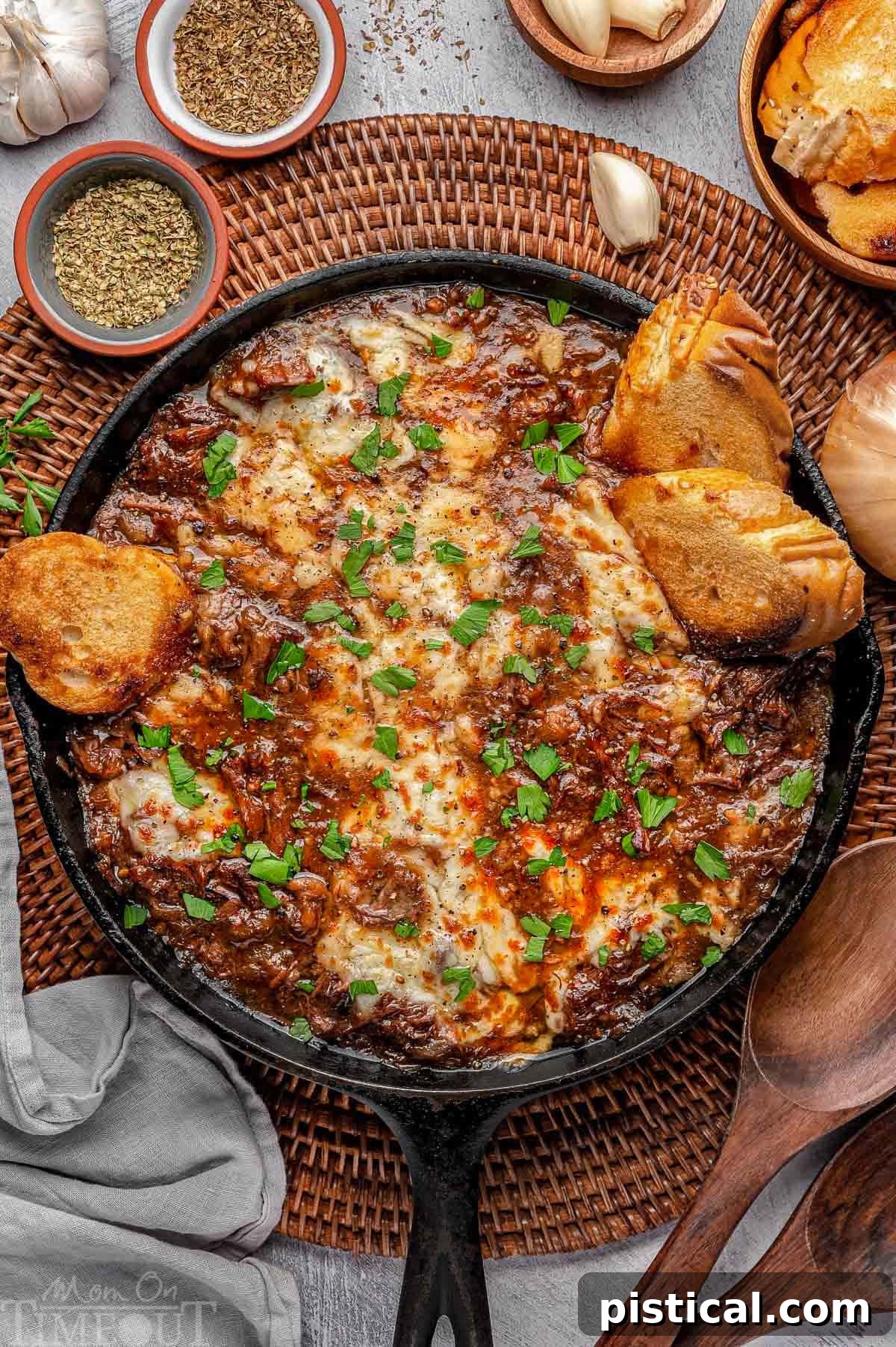 Overhead shot of French Onion Pot Roast in a rustic cast iron skillet, garnished with melted Gruyere cheese and fresh parsley, with golden baguette slices scattered around. Perfect for cozy gatherings.