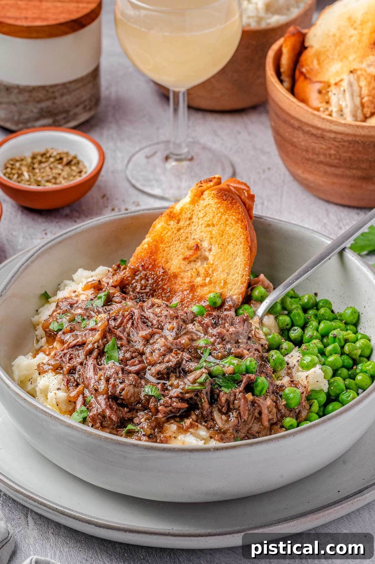 A hearty bowl of French Onion Soup Pot Roast served with creamy mashed potatoes, green peas, and crusty baguette slices, showcasing a complete and comforting meal.