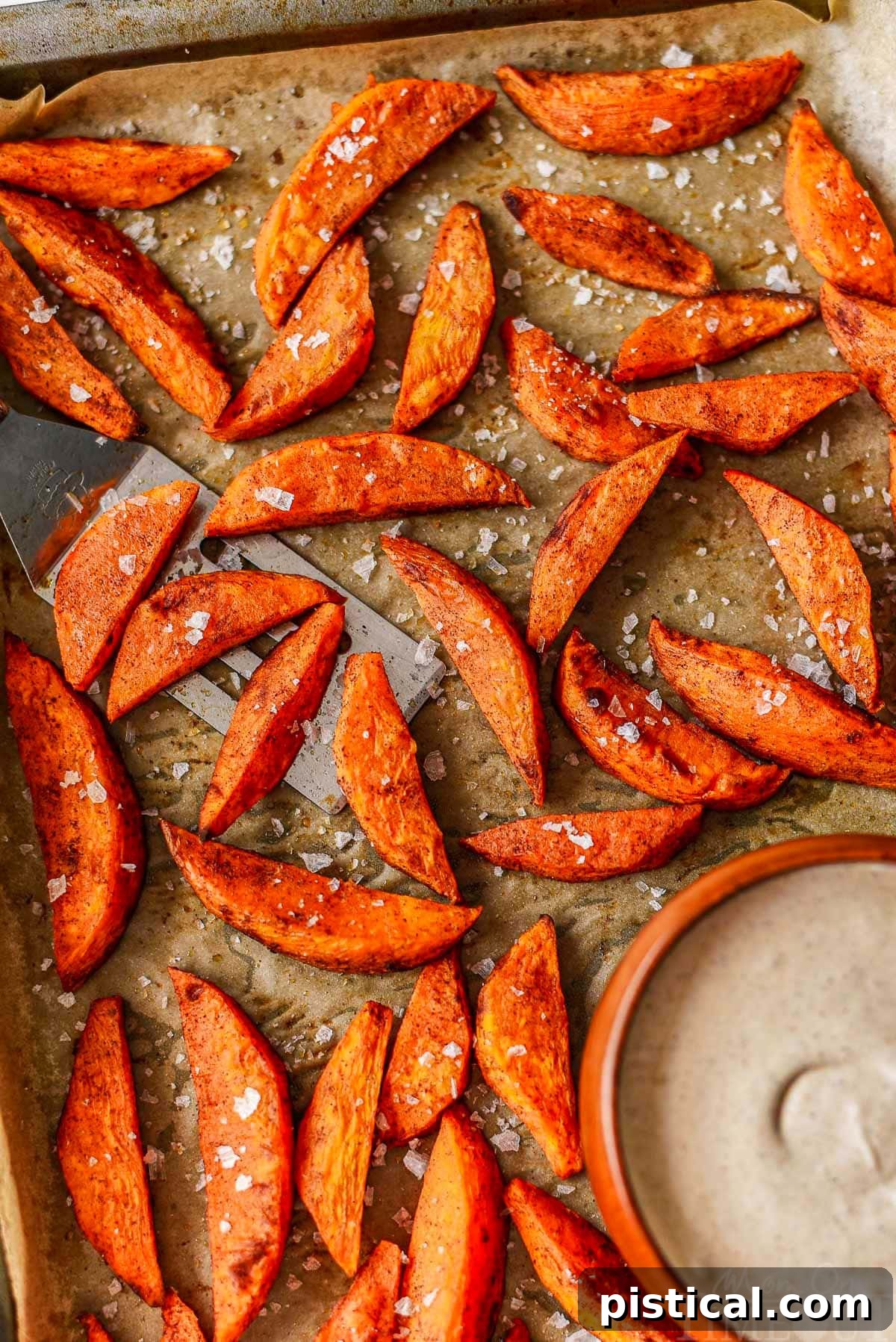 Top-down view of freshly roasted sweet potato wedges on a parchment-lined baking sheet, accompanied by a small bowl of rich brown sugar cinnamon marshmallow dip.