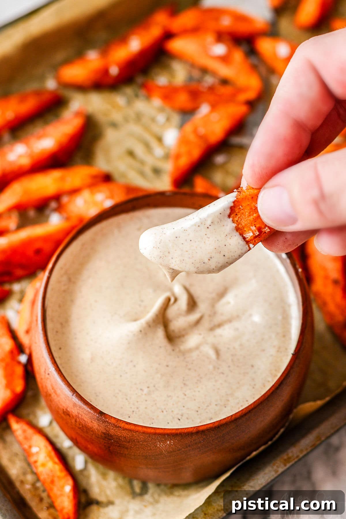 A close-up shot of a crispy sweet potato wedge being dipped into a luscious bowl of cinnamon marshmallow dipping sauce, highlighting the perfect pairing.