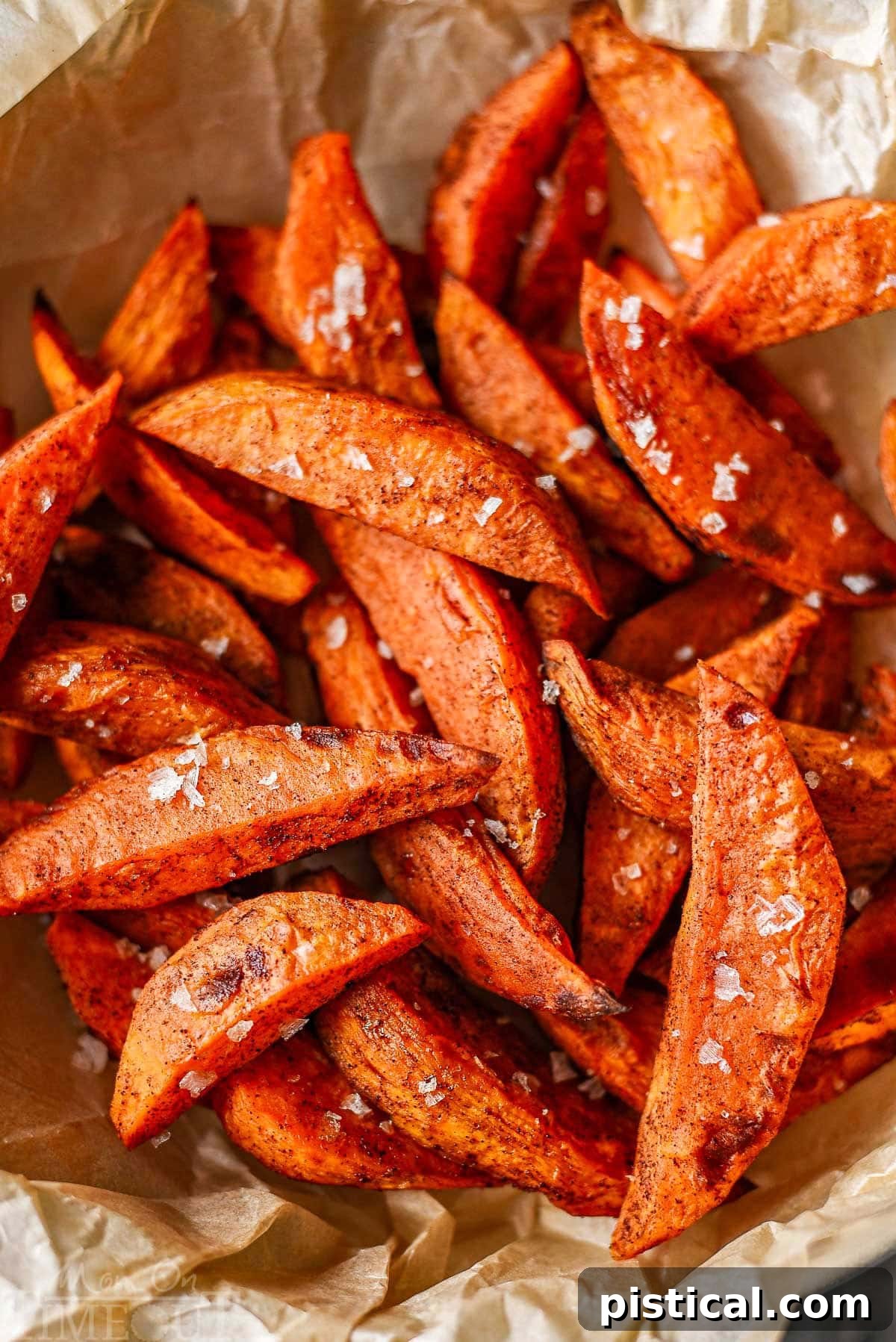 Close-up shot of crispy sweet potato wedges generously sprinkled with flaky sea salt, highlighting their golden texture and enticing appeal.
